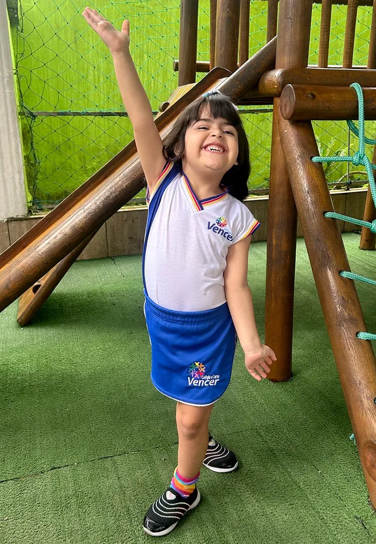 Aluna do Colégio Vencer sorrindo, com o braço erguido, brincando no parquinho